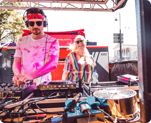 DJs at the 2022 Pride Parade in Vienna, dressed in colorful outfits and carrying rainbow flags, celebrate diversity and equality on a busy street.